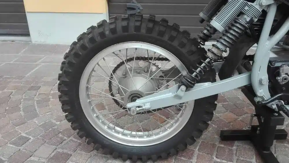 Nahaufnahme des Hinterrads, Stoßdämpfers und Rahmens einer 1976 TGM 250 Cross Motore Villa, restauriert, auf Kopfsteinpflaster