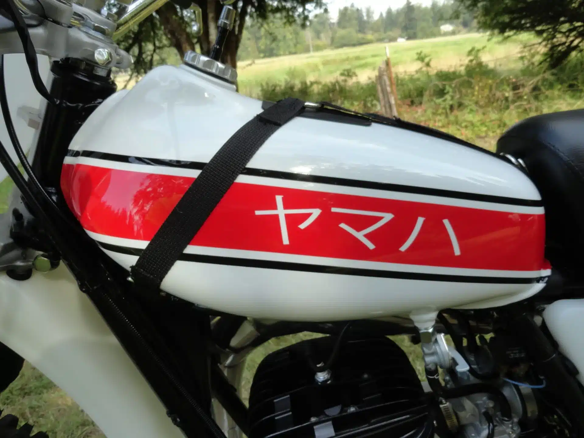 Nahaufnahme des Aluminiumtanks einer 1976 Yamaha YZ250C mit rotem Streifen und japanischem Schriftzug.