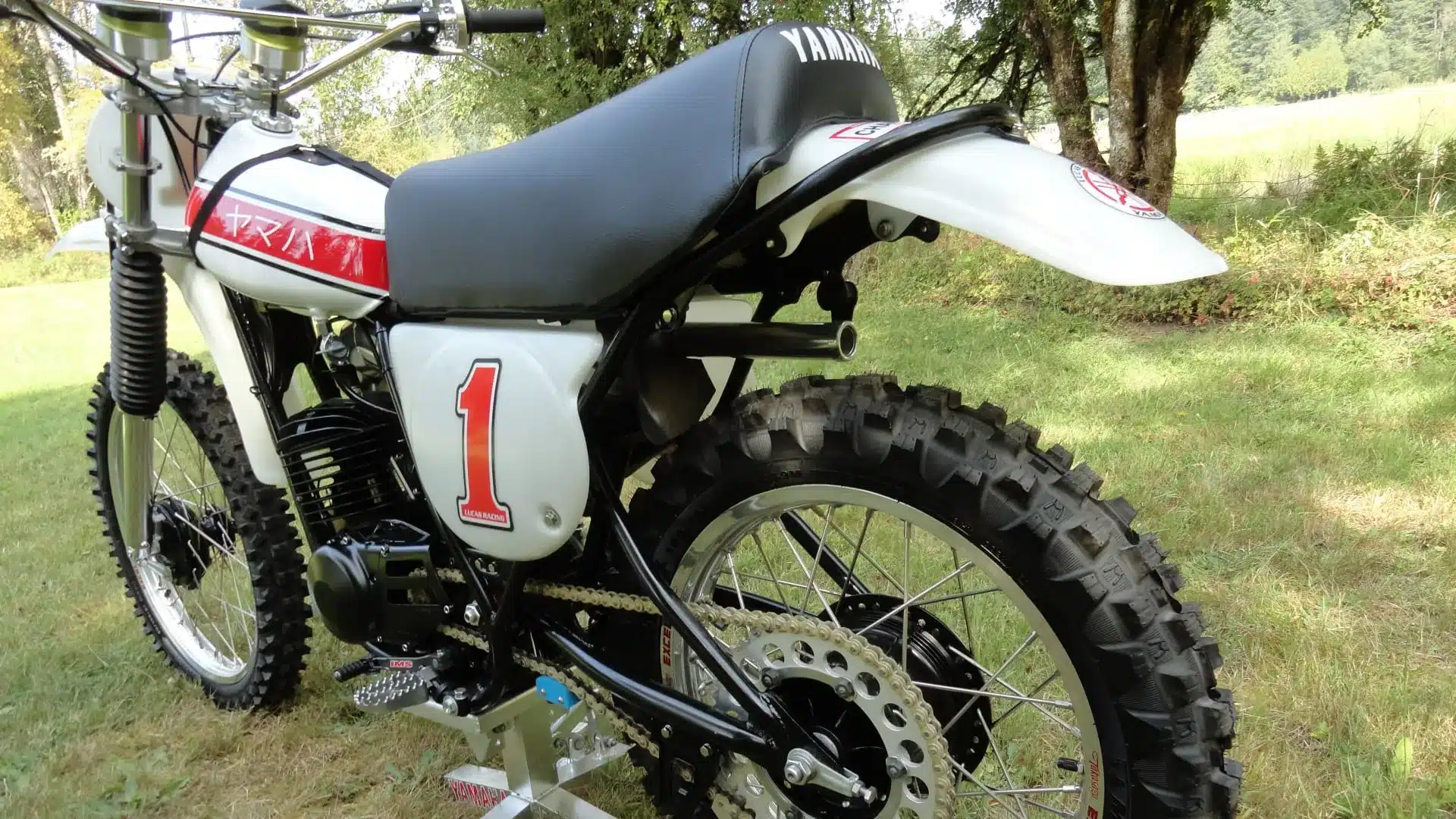 1976 Yamaha YZ250C mit zentralem Federbein und Aluminiumtank, seitlich auf einer Wiese ausgestellt.