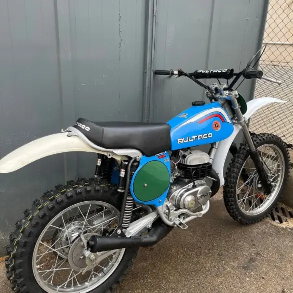 Restaurierte blaue Bultaco Pursang MK10 250cc von 1977, Seitenansicht vor grauer Wand.