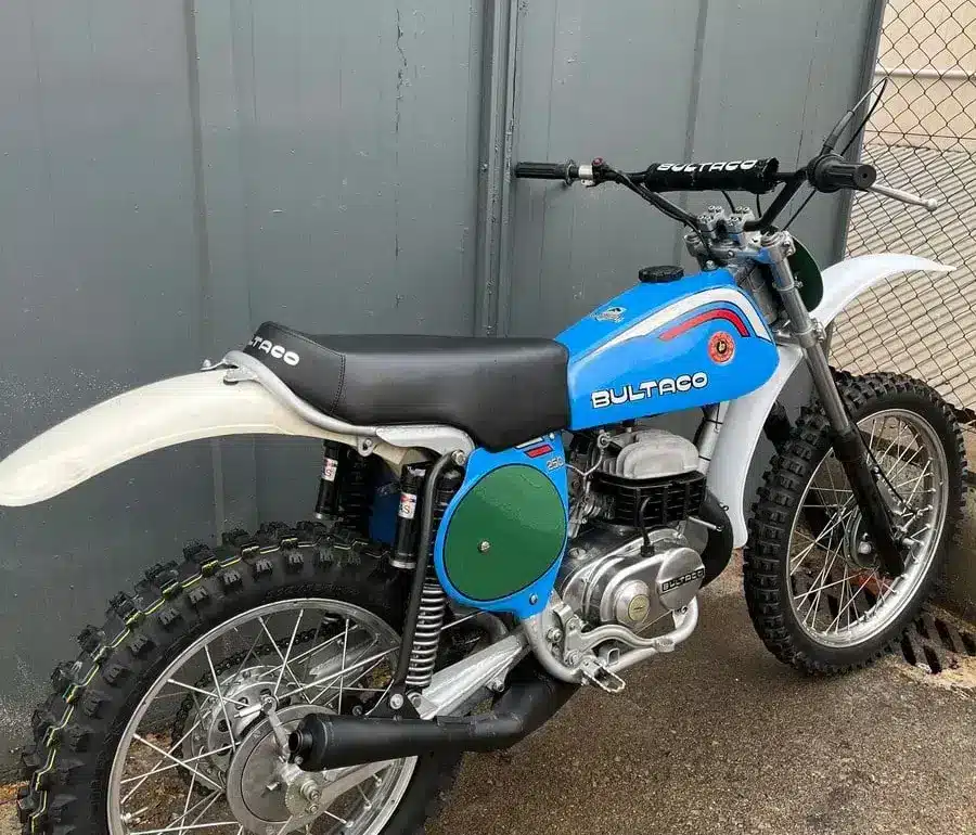 Restaurierte blaue Bultaco Pursang MK10 250cc von 1977, Seitenansicht vor grauer Wand.