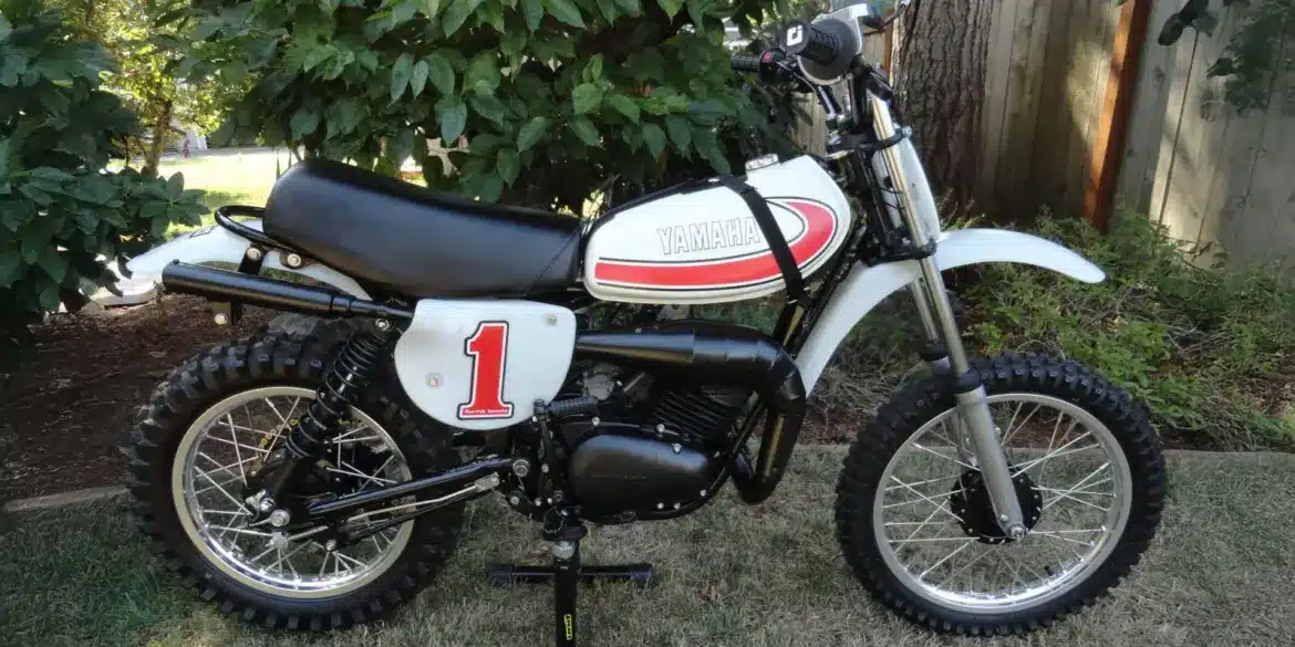 Seitliche Gesamtansicht einer 1977 Yamaha YZ80D Motocross-Maschine mit Startnummer 1, aufgestellt im Garten.