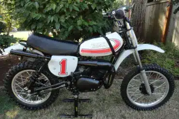 Seitliche Gesamtansicht einer 1977 Yamaha YZ80D Motocross-Maschine mit Startnummer 1, aufgestellt im Garten.