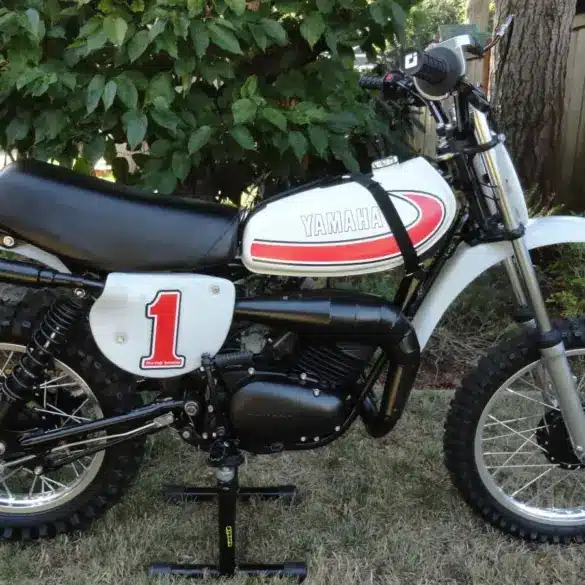 Seitliche Gesamtansicht einer 1977 Yamaha YZ80D Motocross-Maschine mit Startnummer 1, aufgestellt im Garten.