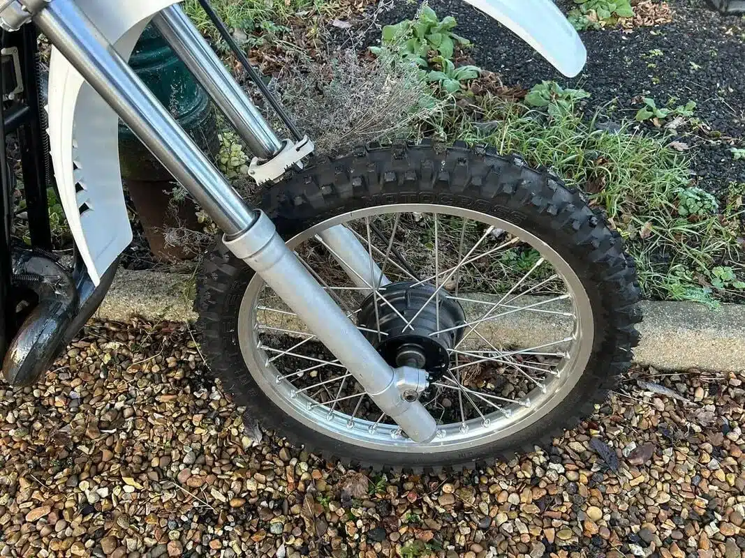 Vorderrad und Gabel einer weißen Yamaha YZ400E aus dem Baujahr 1978 auf Kiesuntergrund.