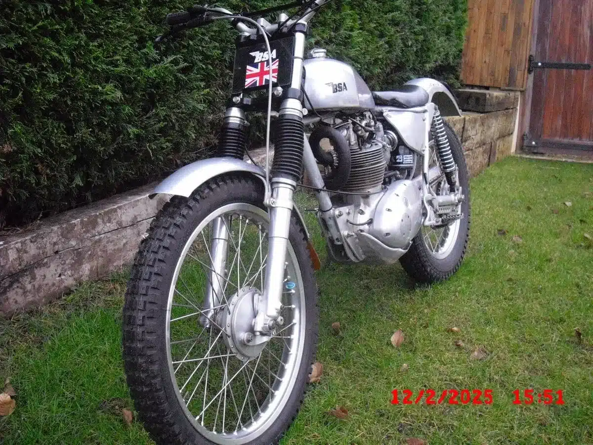 Seitenansicht einer silbernen BSA B40 Trials Special von 1963 mit grobstolligen Reifen im Garten, vorderer Bereich im Fokus.
