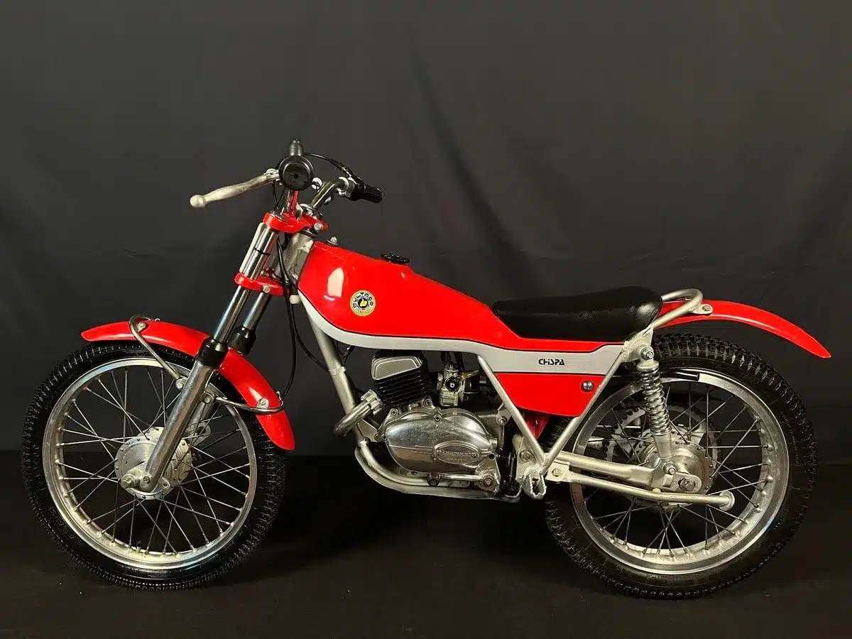 Seitenansicht einer restaurierten Bultaco Chispa 50 von 1980 in Rot vor neutralem Hintergrund.
