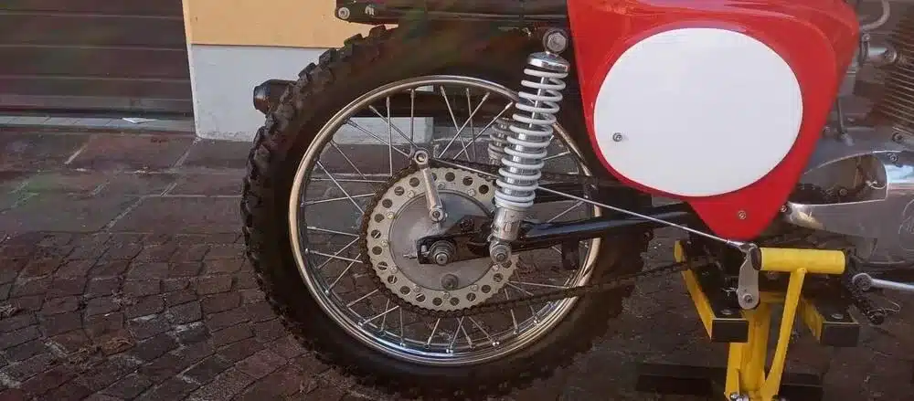 Das Hinterrad einer Gilera‑Bessone 175 aus dem Jahr 1970, restauriert, mit sichtbarer Kette und Federbein, Ausschnittansicht.