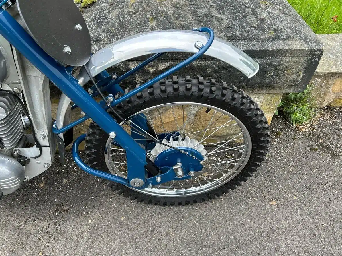 Nahaufnahme des vorderen Rads, Rahmens und Motors einer blauen Greeves Hawkstone MCS 250cc von 1960 mit Stollenreifen und Aluminium-Bremstrommel.