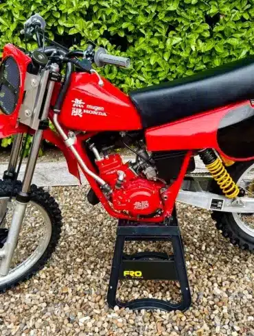 Rote Honda CR 125 von 1980 mit Mugen-Banzai-Konversion, Aluminiumtank, Öhlins-Federbeinen und am Gabeljoch montiertem Kühler, seitlich fotografiert.
