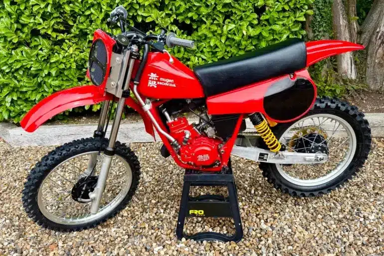 Rote Honda CR 125 von 1980 mit Mugen-Banzai-Konversion, Aluminiumtank, Öhlins-Federbeinen und am Gabeljoch montiertem Kühler, seitlich fotografiert.