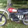 Seitenansicht einer Husqvarna 250 Cross von 1967 mit rotem Tank und Startnummer 33 auf grasbewachsenem Untergrund