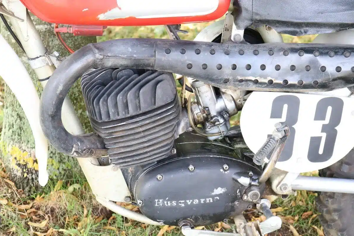 Seitliche Detailansicht des luftgekühlten Einzylinder-Zweitaktmotors einer Husqvarna 250 Cross von 1967 mit sichtbarem Auspuff und Startnummernschild