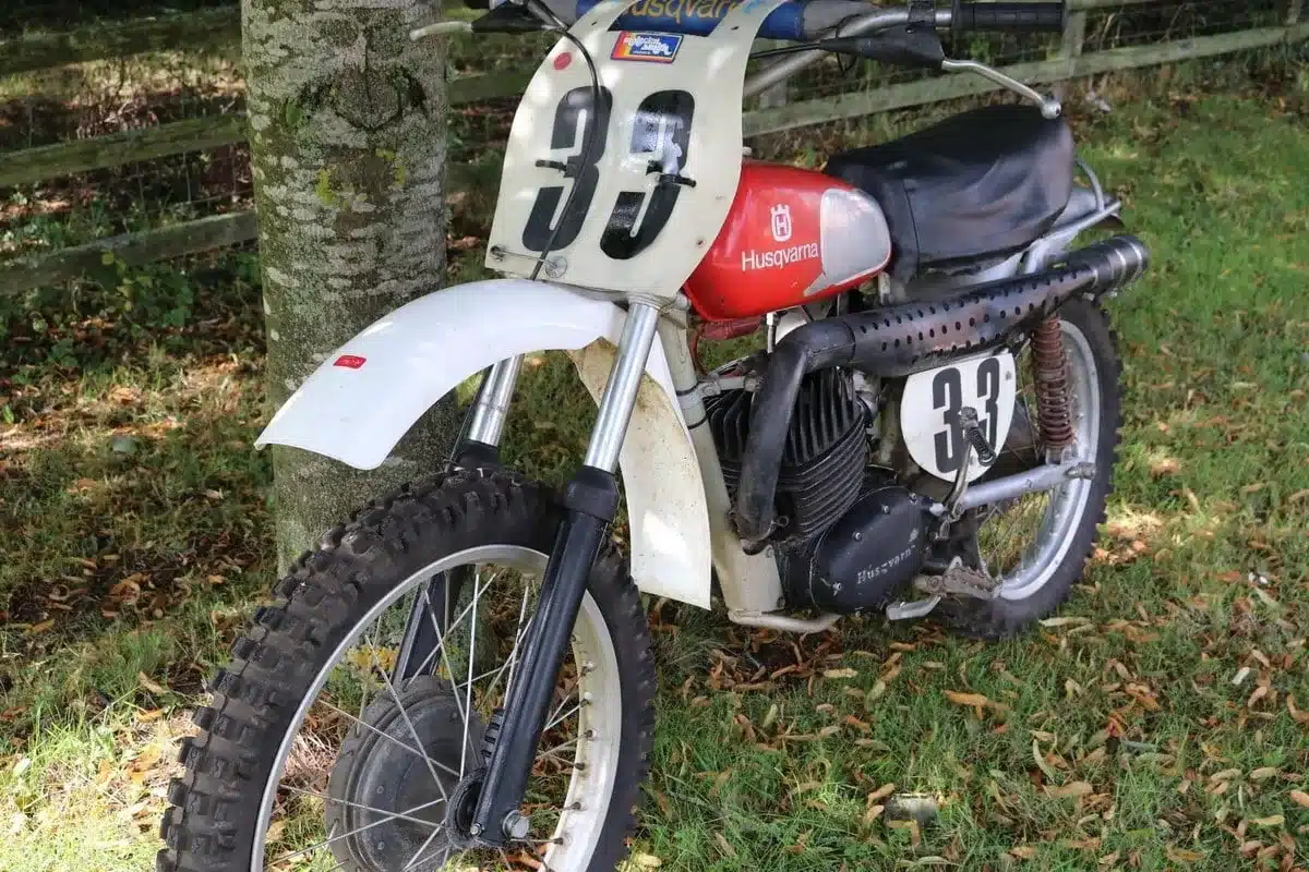 Husqvarna 250 Cross Baujahr 1967 mit rotem Tank, Twin-Shock-Hinterradfederung, Stollenreifen und Startnummer 33 im Freien stehend.