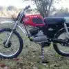 Seitenansicht einer roten Kawasaki F2 175 aus dem Jahr 1967 auf einer Wiese, Offroad-Bereifung, klassisches Design