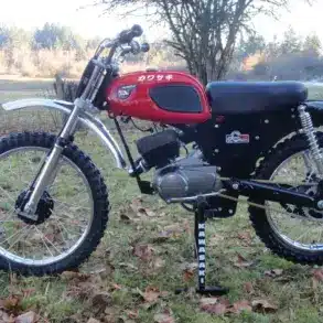 Seitenansicht einer roten Kawasaki F2 175 aus dem Jahr 1967 auf einer Wiese, Offroad-Bereifung, klassisches Design