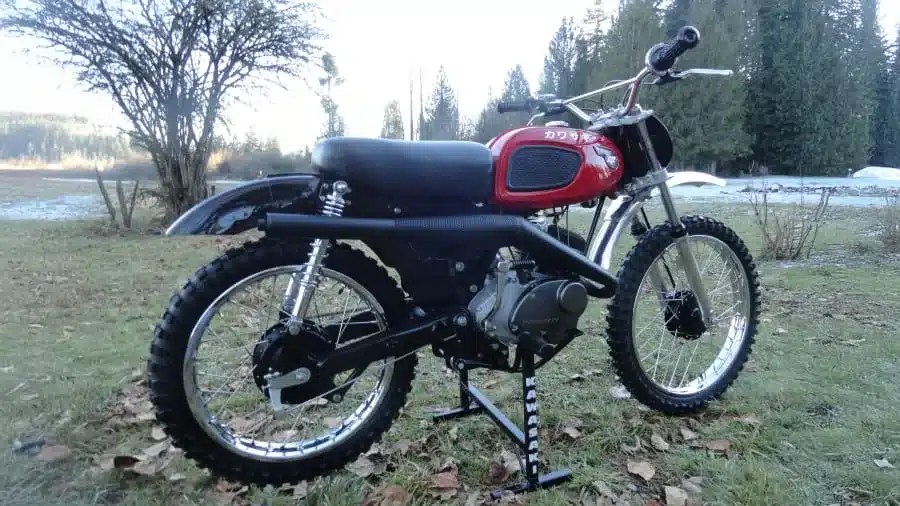 Seitenansicht einer roten Kawasaki F2 175 von 1967 im Gelände, Offroad-Bereifung, auf Motorradständer.