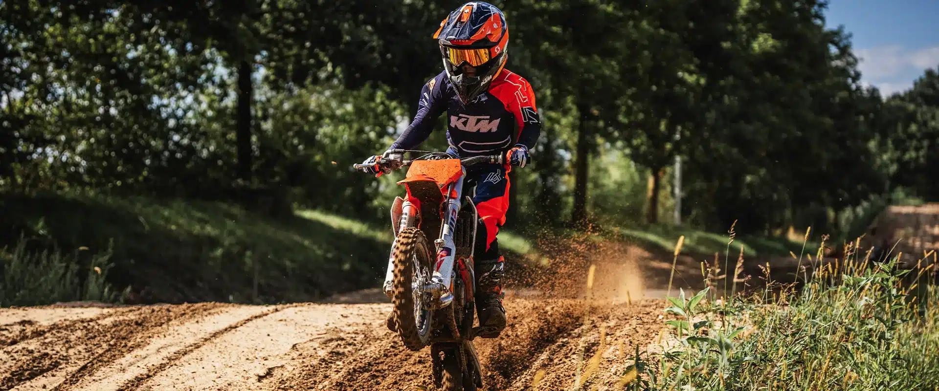 Kind fährt die KTM 50 SX 2026 im Motocross-Gelände, hebt das Vorderrad an und trägt vollständige KTM-Motocross-Ausrüstung.
