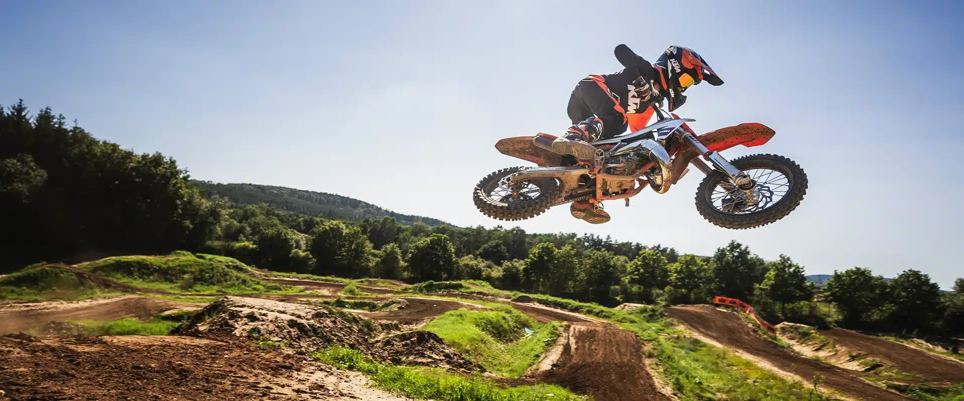 KTM 65 SX 2026 Motocross-Motorrad mit jugendlichem Fahrer in voller Montur bei einem Sprung auf einer Offroad-Strecke.