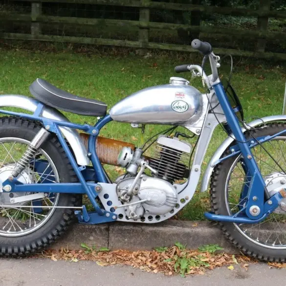 Trial-Motorrad mit gelbem Federbein, silbernem Tank und grobstolligen Reifen, geparkt am Straßenrand