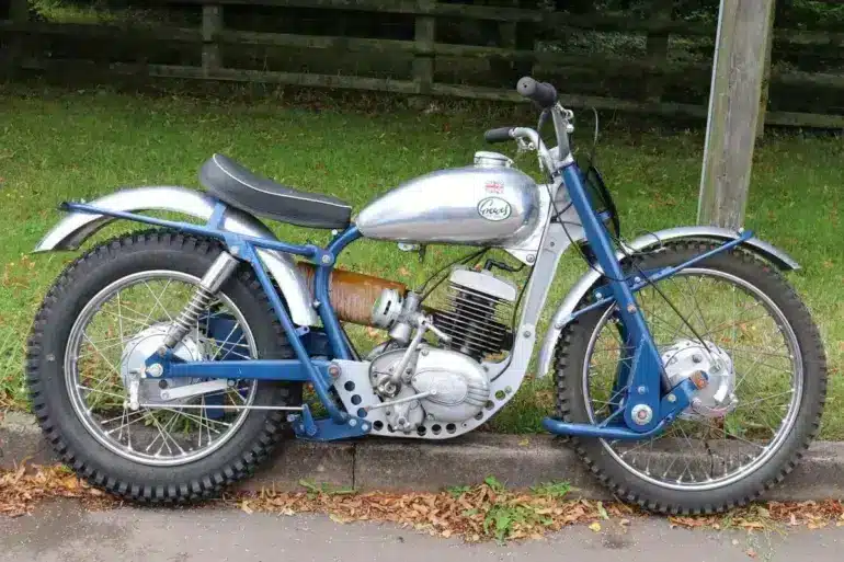 Trial-Motorrad mit gelbem Federbein, silbernem Tank und grobstolligen Reifen, geparkt am Straßenrand