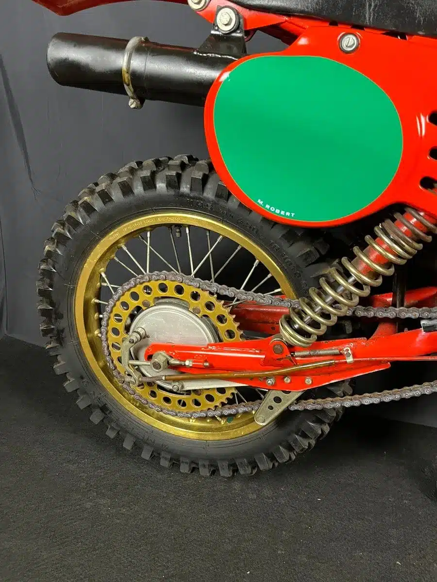 Nahaufnahme des Hinterrads einer roten Maico MC 250 von 1980 mit goldener Felge, Federbein und grünem Startnummernschild