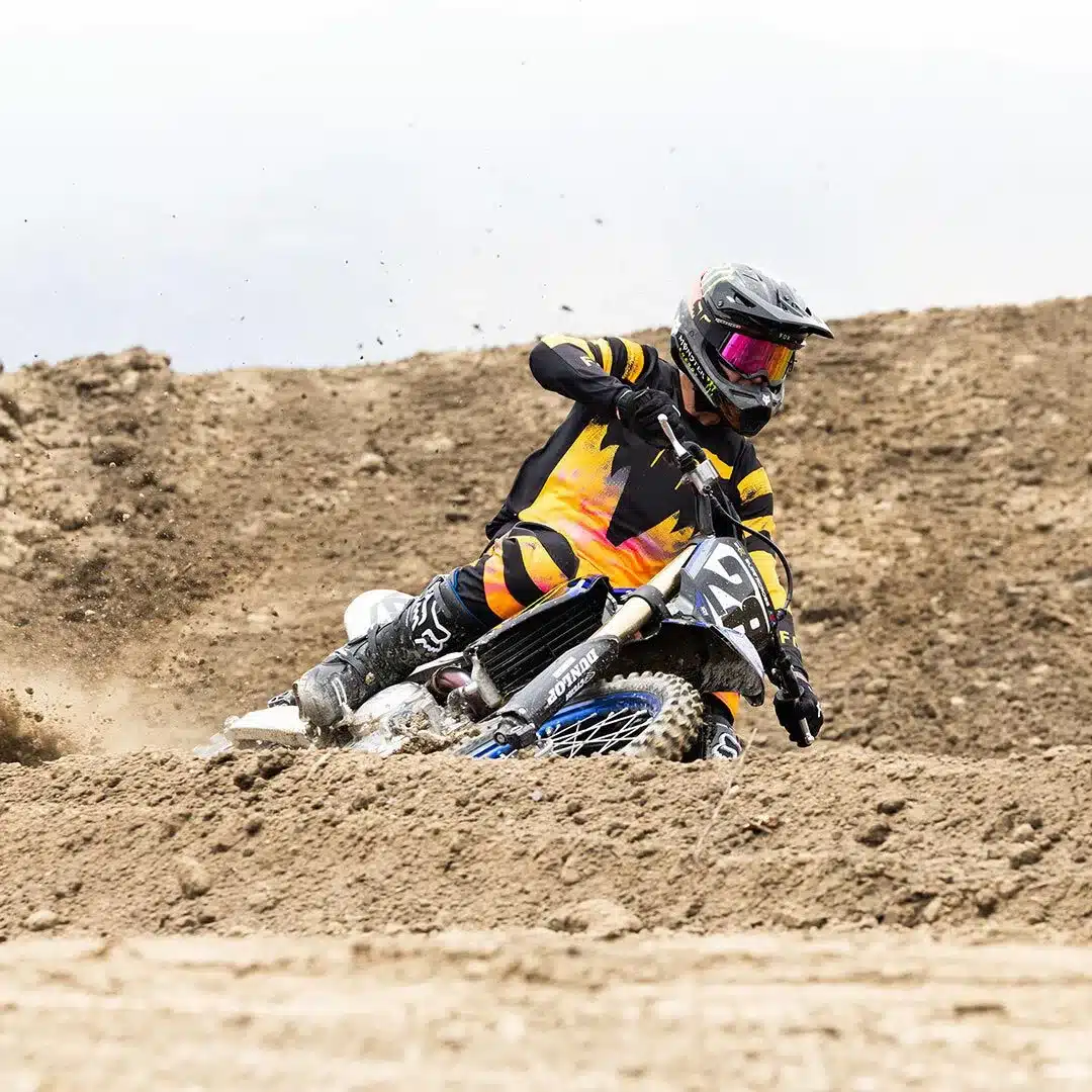 Motocross-Fahrer mit verspiegelter Schutzbrille und bunter Bekleidung auf sandiger Strecke