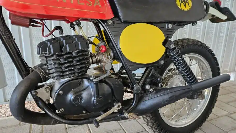 Motor und Fahrwerk einer Montesa Enduro 250 (1975) in Nahaufnahme, mit sichtbaren Details wie Auspuff, Federbein und Rahmen.