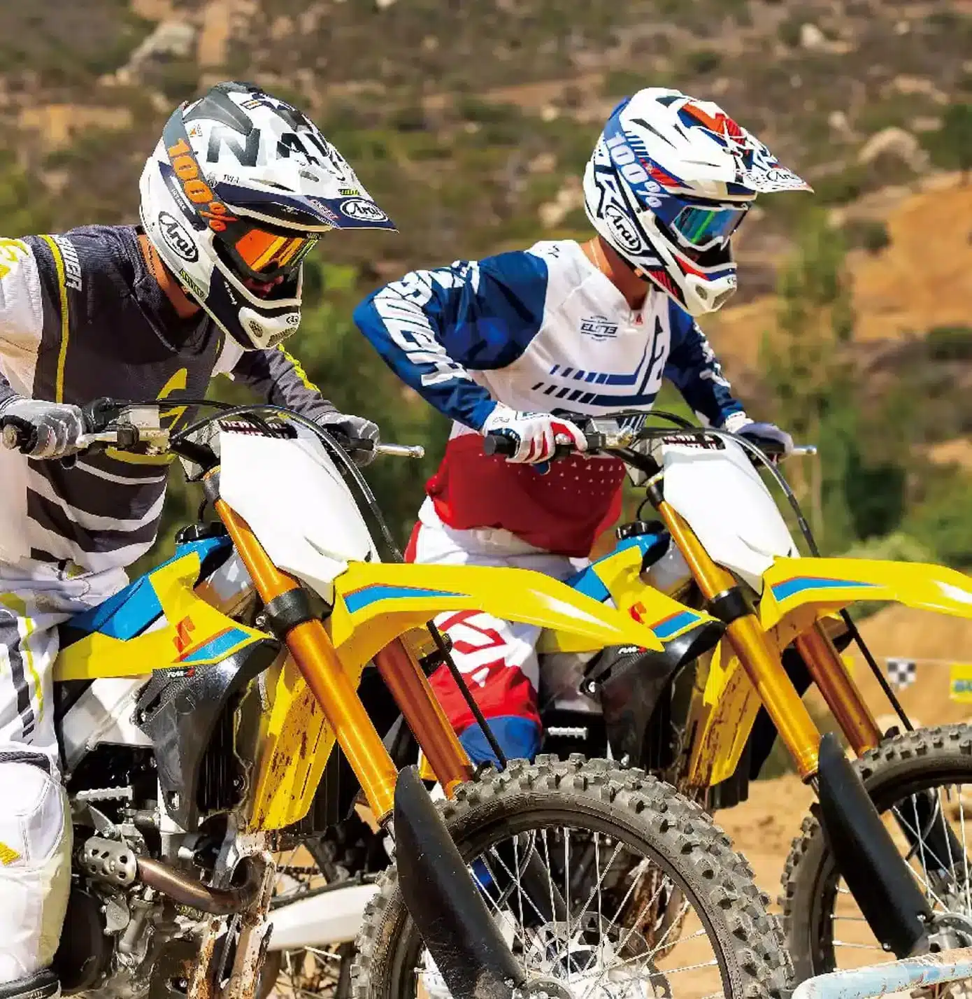 Zwei Suzuki RM-Z250 Motorräder mit Fahrern in kompletter MX-Ausrüstung beim Start auf einer Offroad-Piste.