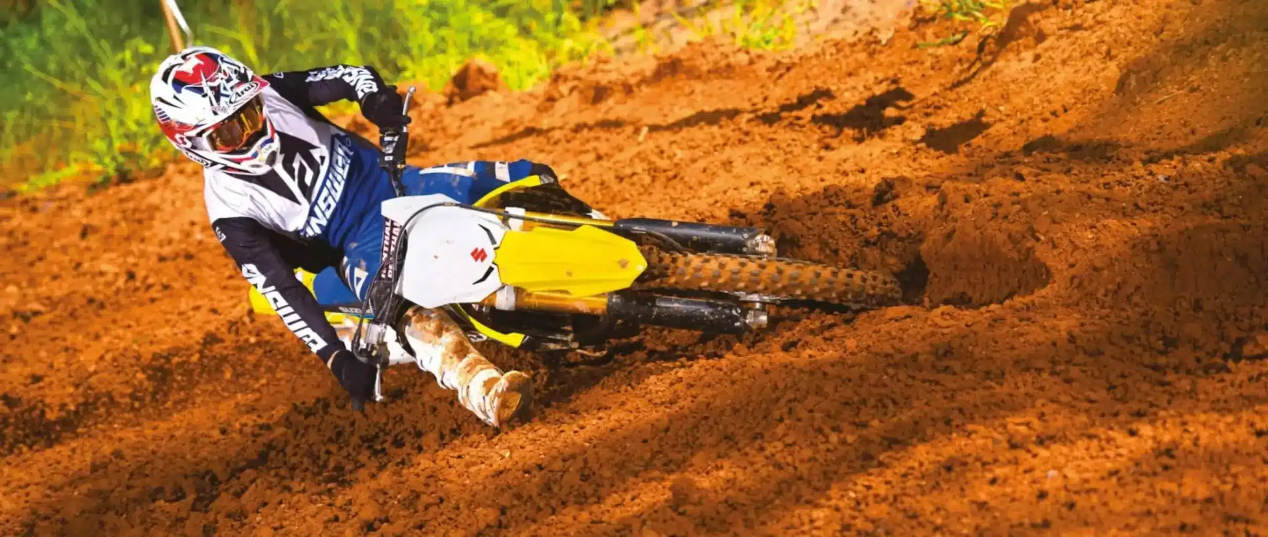 Motocross-Fahrer auf Suzuki RM-Z250 beim Kurvenfahren auf sandiger Strecke.