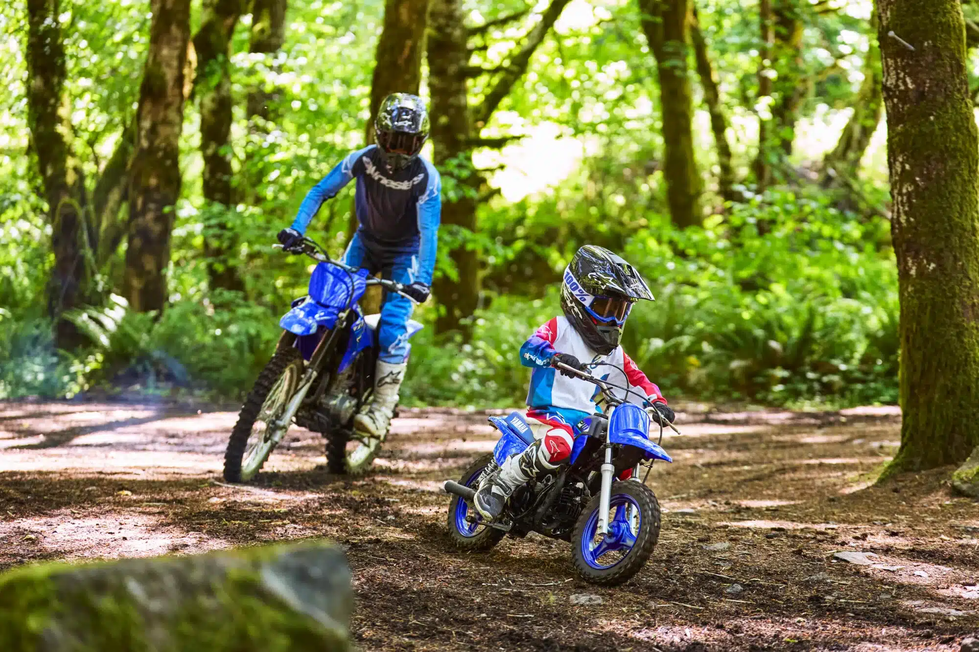 Kind auf Yamaha PW50 im Wald, begleitet von Erwachsenem auf Motorrad