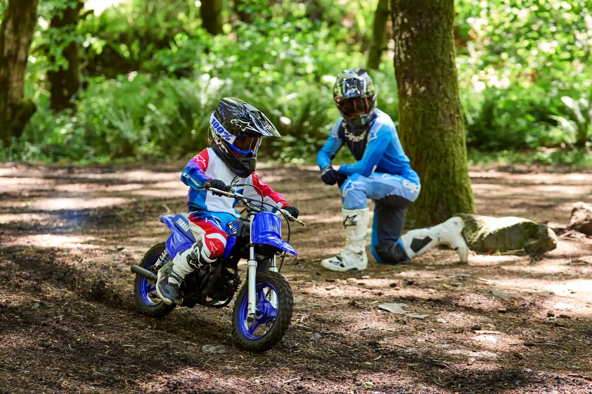 Kind auf Yamaha PW50 Motorrad mit Begleitperson im Wald beim Offroad-Fahren.