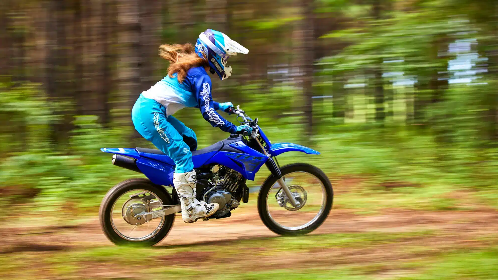Jugendliche fährt Yamaha TT-R125 auf einem Waldweg, Seitenansicht in Bewegung