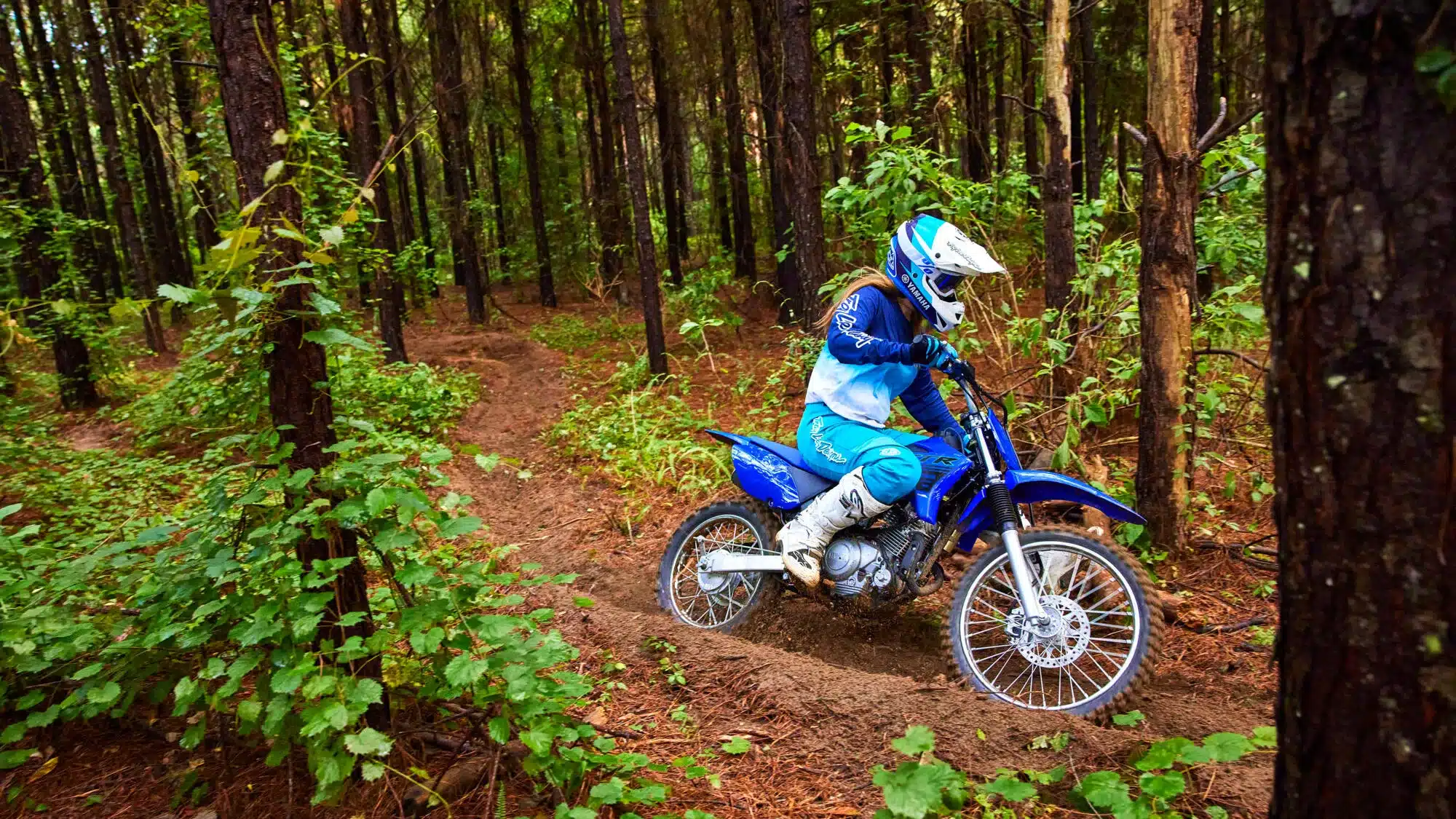 Motorradfahrer auf einer blauen Yamaha TT-R125 fährt durch einen bewaldeten Offroad-Trail.