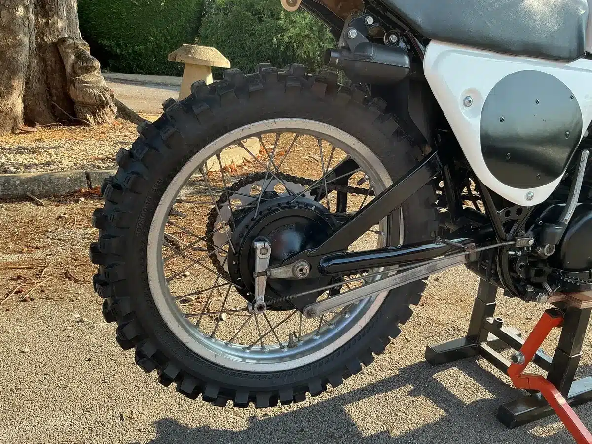 Nahaufnahme des Hinterrads und der Monoshock-Federung einer Yamaha YZ 360B von 1975, abgestellt auf einem Ständer im Freien.