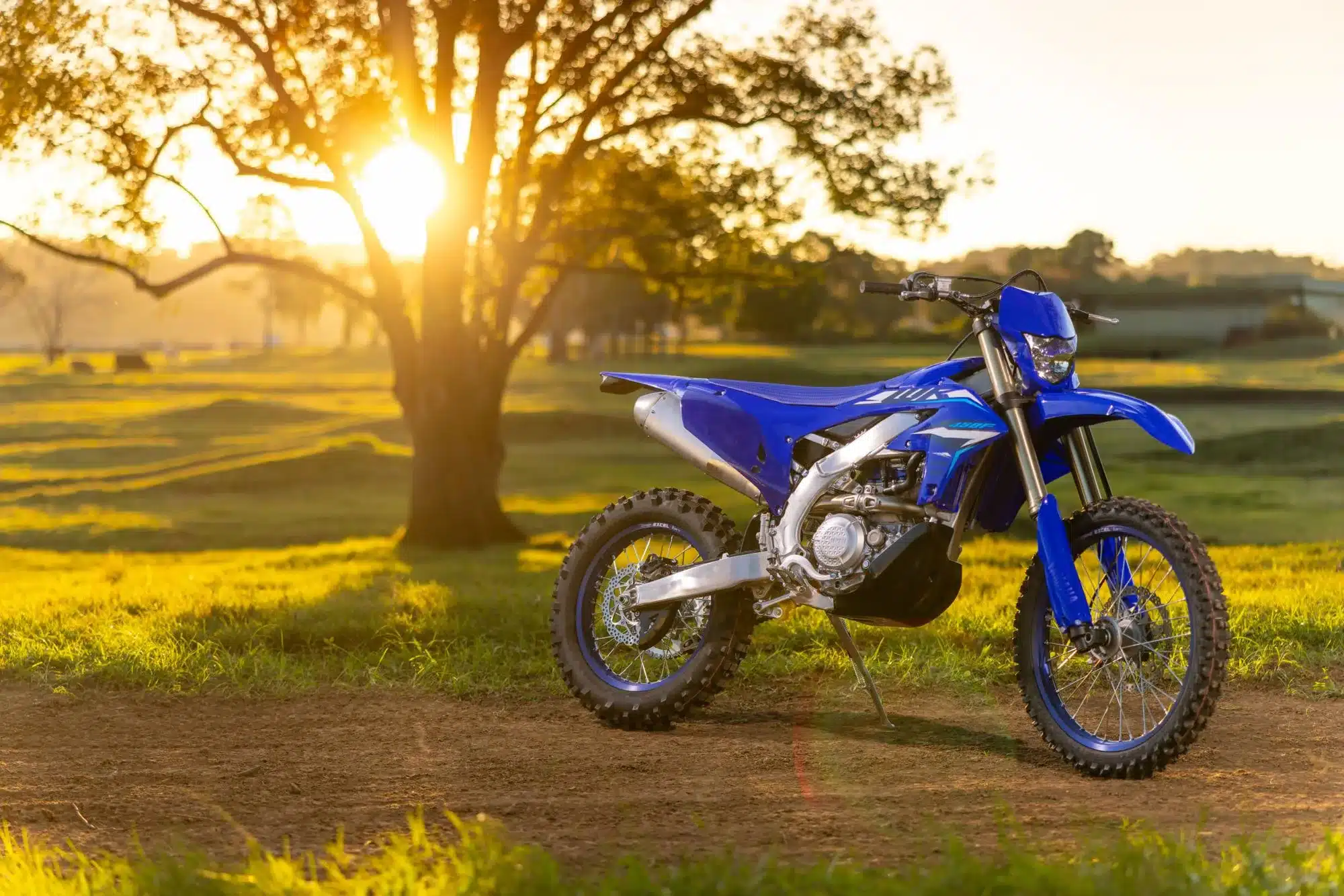 Yamaha YZ125 Zweitakt-Motocross-Motorrad in blauer Lackierung seitlich auf einer Offroad-Strecke bei Sonnenuntergang.