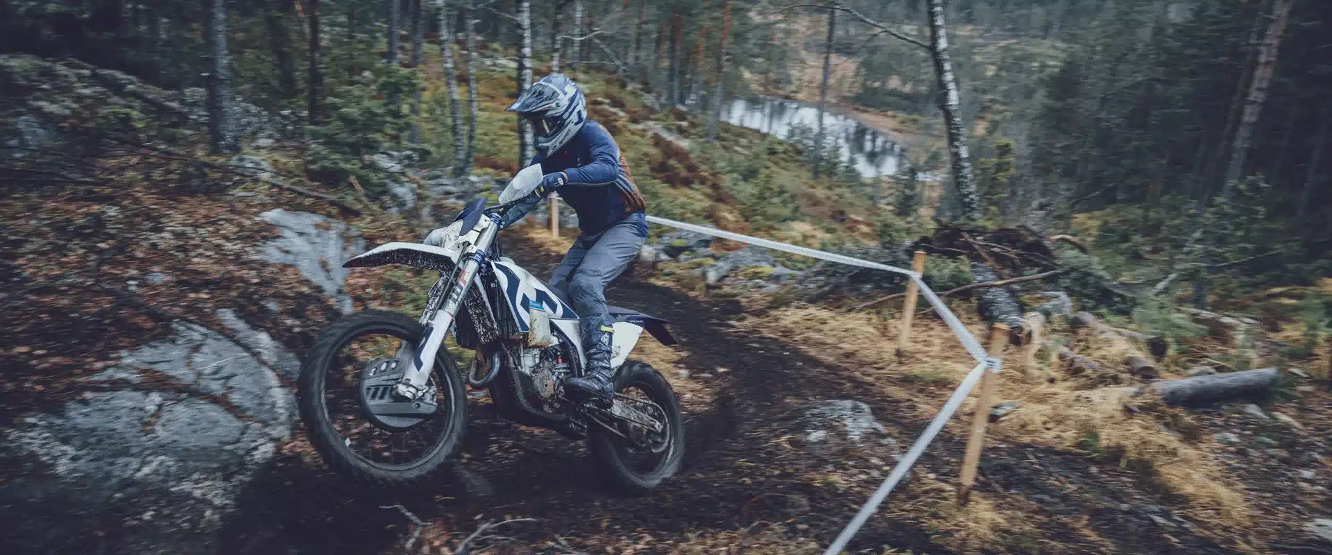 Fahrer auf Husqvarna FE 350 Enduro-Motorrad bei Offroad-Wettkampf im Wald, steiler Anstieg und matschiges Terrain.