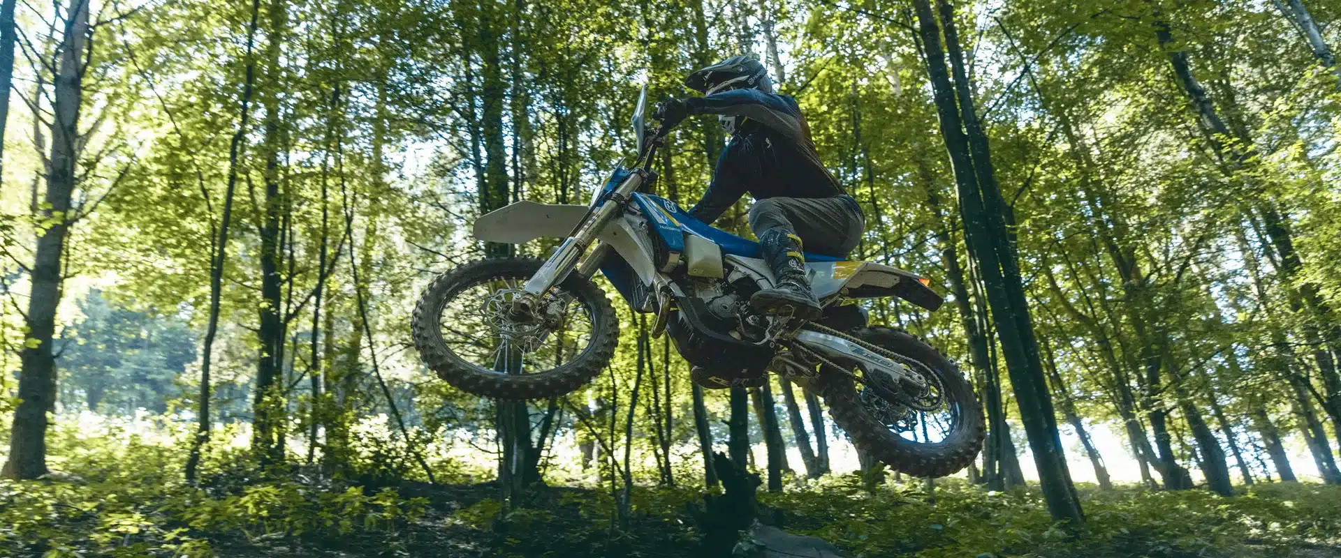 Husqvarna FE 450 Heritage 2025 springt mit Fahrer im Endurounterholz über eine Geländestufe.