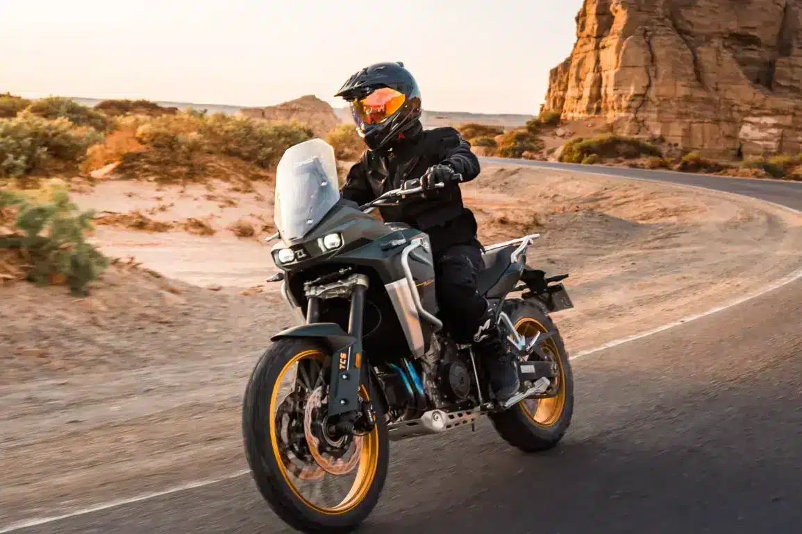 KOVE 800X PRO Adventure-Motorrad fährt auf einer asphaltierten Straße durch felsige Wüstenlandschaft