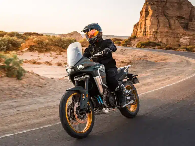 KOVE 800X PRO Adventure-Motorrad fährt auf einer asphaltierten Straße durch felsige Wüstenlandschaft