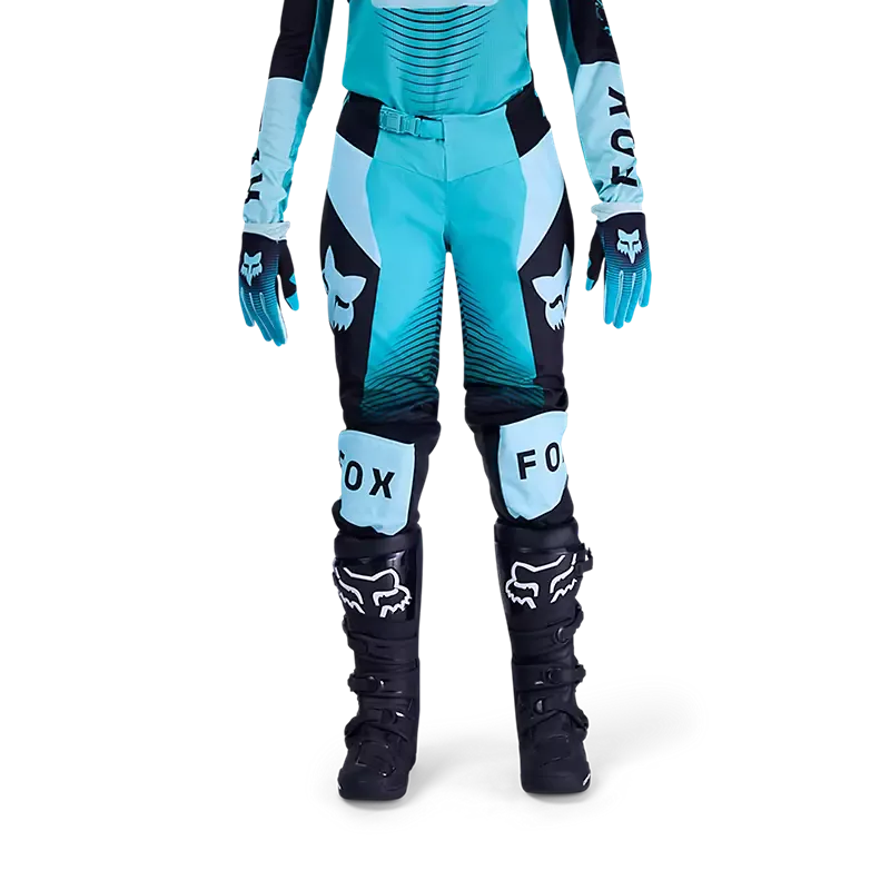 Frau trägt die 180 Collect Motocross-Hose von Fox Racing in Türkis und Schwarz mit typischen FOX-Grafiken.