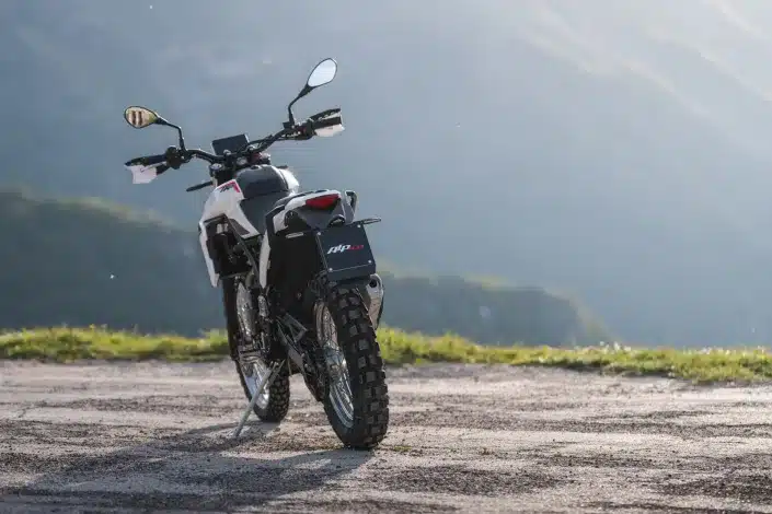 Beta Alp 4.0 Enduro-Motorrad von hinten mit Geländebereifung und LED-Rückleuchte auf einem Schotterweg vor Berglandschaft.