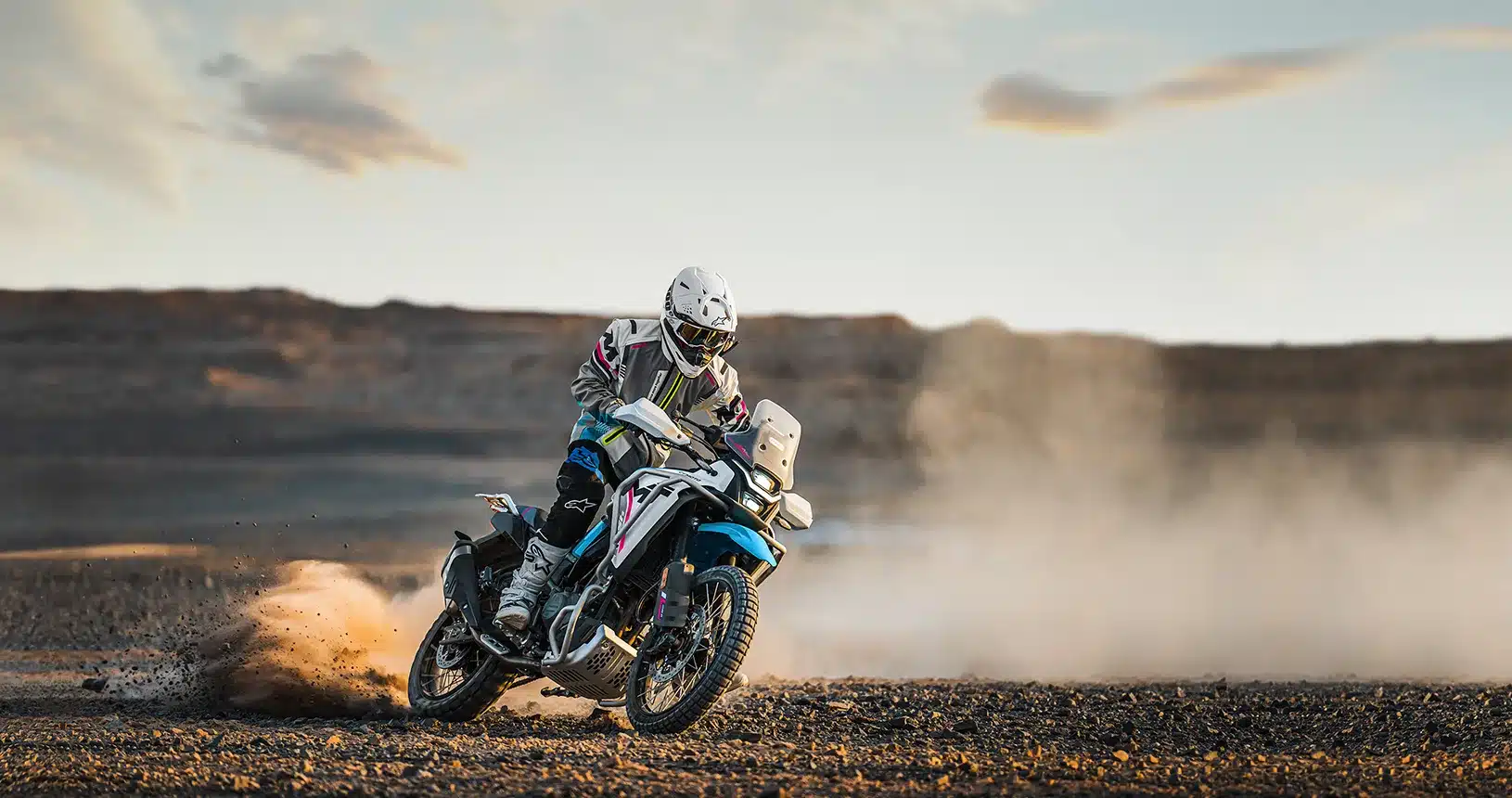 CFMoto 450MT fährt quer durch eine staubige Landschaft im Gelände, Actionfoto mit Fahrer in voller Ausrüstung.