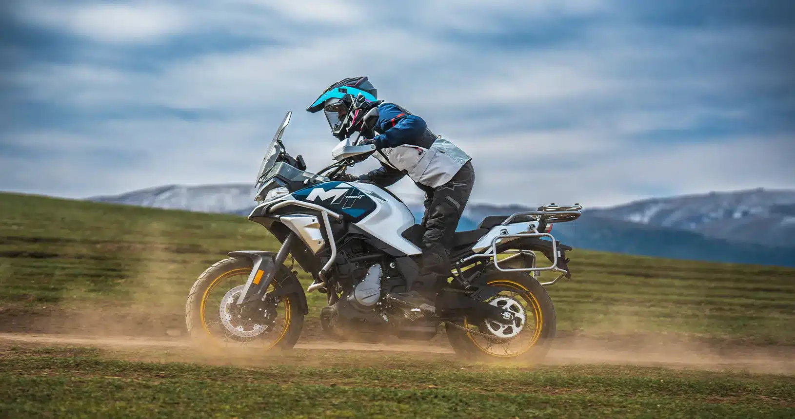 CFMOTO 700MT Motorrad fährt mit Fahrer im Enduro-Outfit durch eine landschaftliche Kulisse auf unbefestigtem Untergrund.