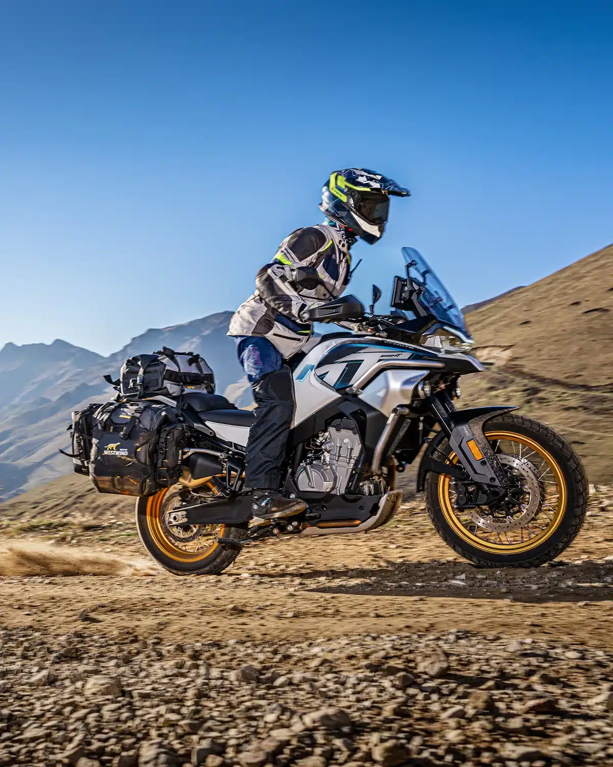 CFMOTO 800MT Explore Motorrad mit Gepäck auf Schotterstraße in bergiger Landschaft.