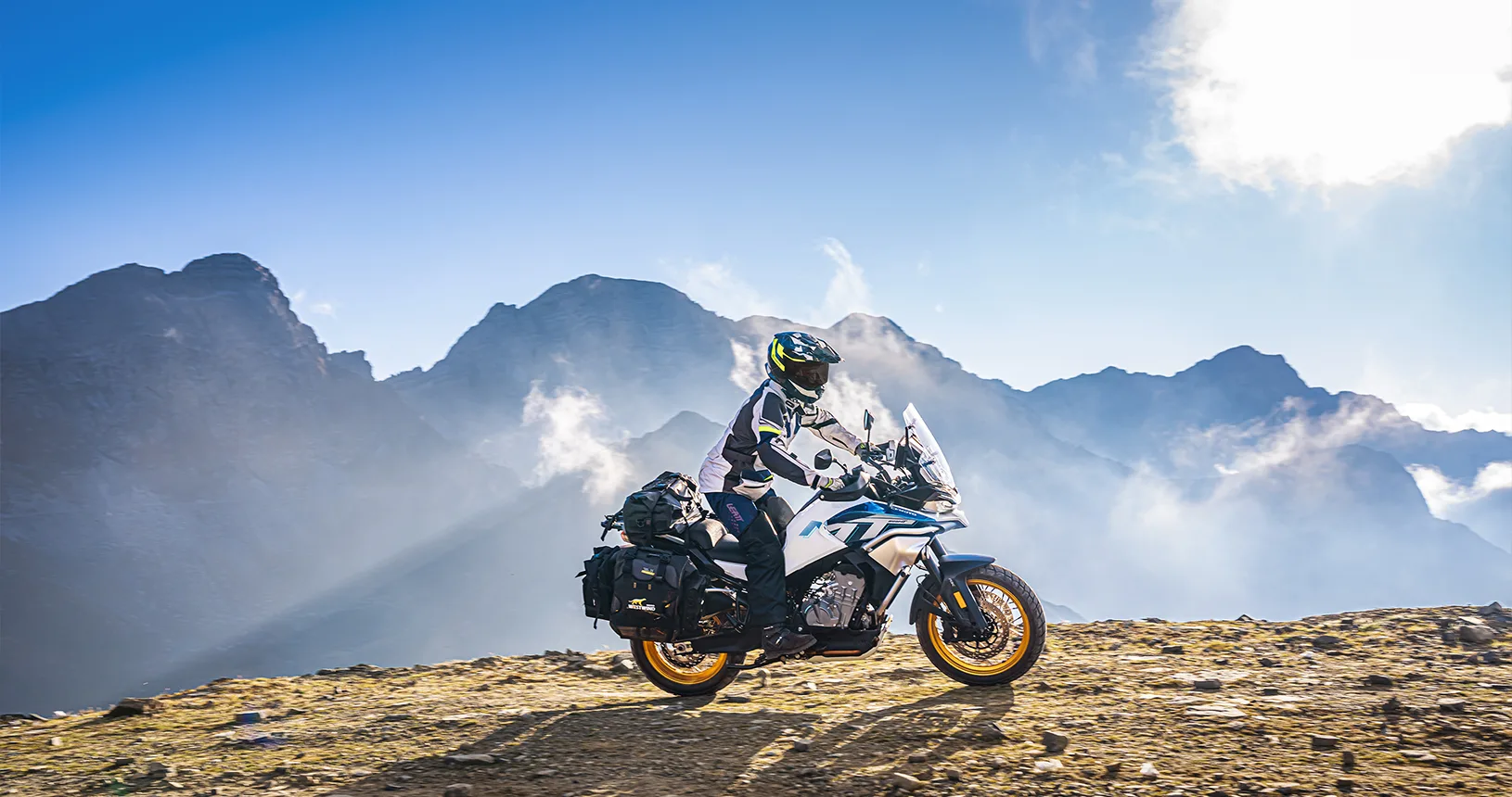 CFMOTO 800MT Explore mit Gepäck, gefahren von einer Person in Motorradkleidung, in den Bergen.