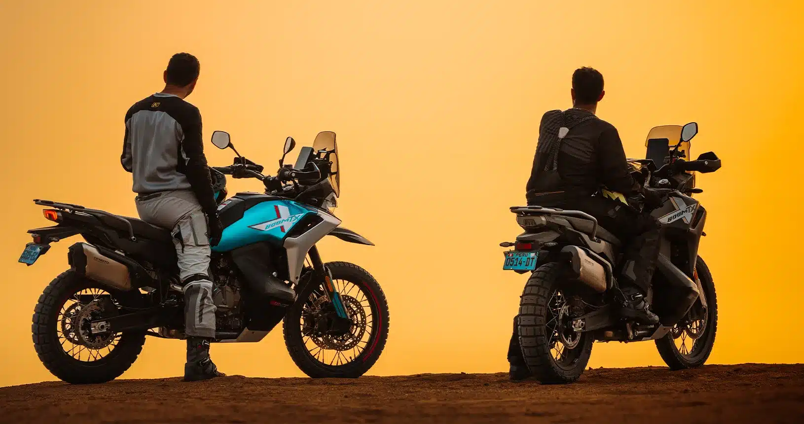 Zwei CFMoto 800MT-X Motorräder mit Fahrern auf einem Hügel vor orangefarbenem Himmel