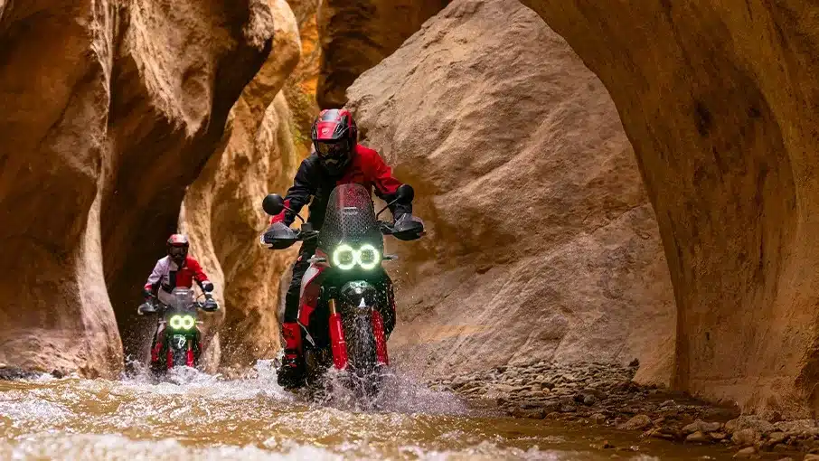 Zwei Ducati DesertX Rally Motorräder fahren durch eine enge Schlucht mit Wasser und Felsen.