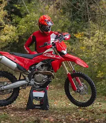 Ducati Desmo450 EDS Enduro-Motorrad in einer herbstlichen Waldumgebung mit Fahrer in roter Ausrüstung.