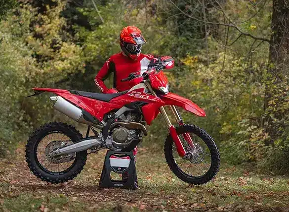 Ducati Desmo450 EDS Enduro-Motorrad in einer herbstlichen Waldumgebung mit Fahrer in roter Ausrüstung.